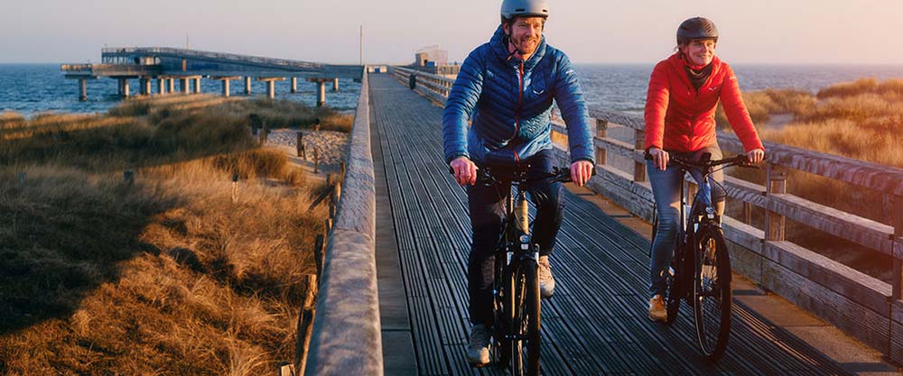 Couple riding two Merida electric hybrid bikes down wharf