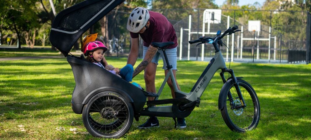 Couple riding two electric hybrid bikes with bike trailer attached