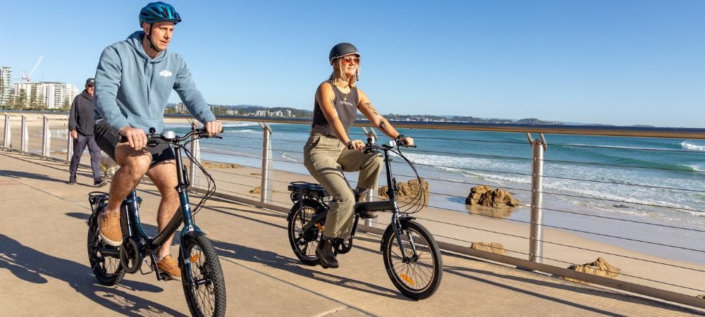 Couple riding two electric foldable bikes at the beach