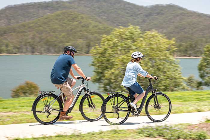 Senior citizens riding Merida e-commuter bikes along bike pathway beside Australian lake